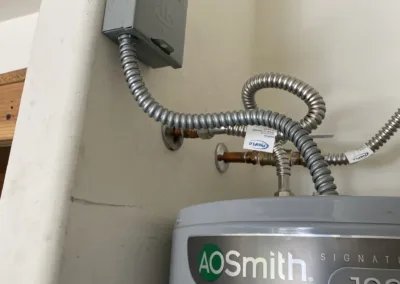 Metal conduit pipes connected to an electrical box above a water heater.